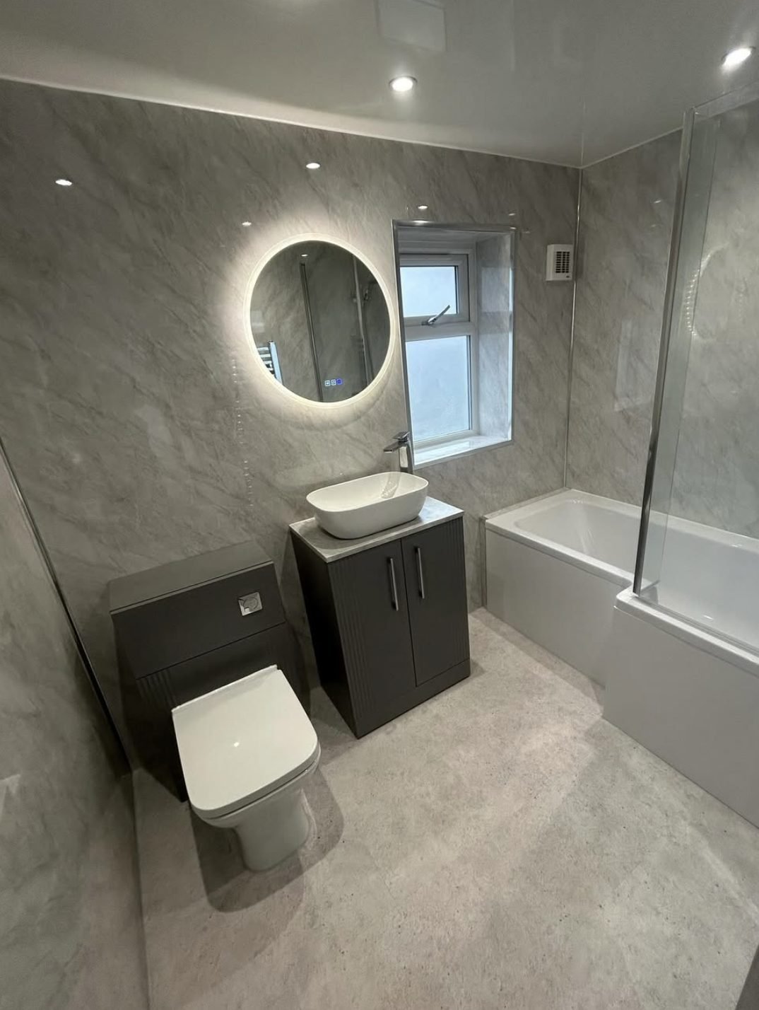 Grey marble effect panelled bathroom with backlit round mirror and dark vanity